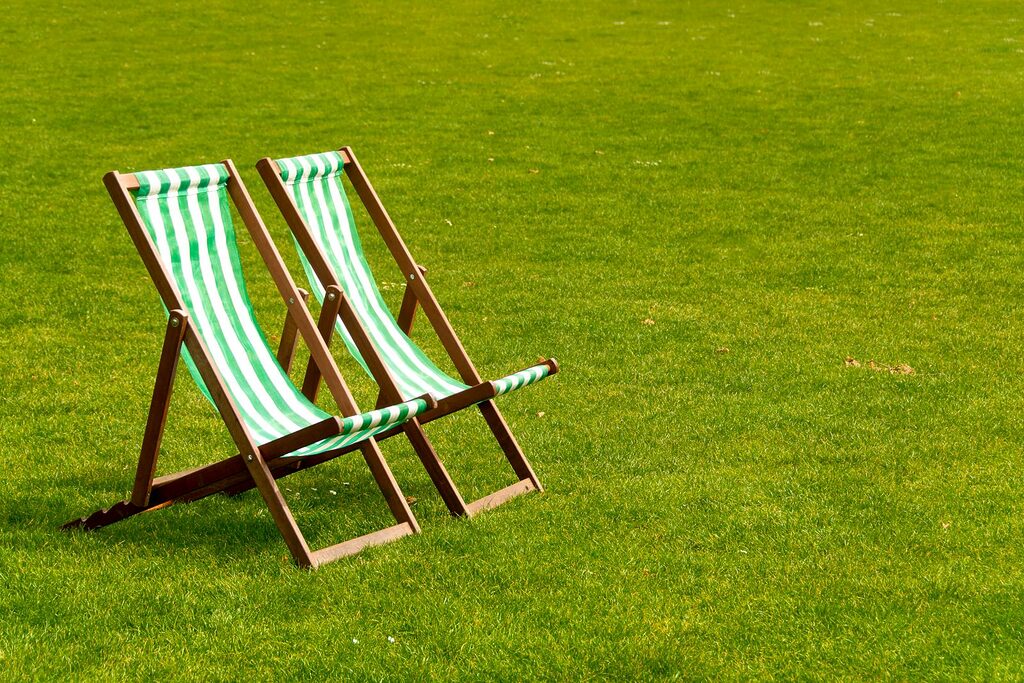 Two striped deck chairs on a lush green lawn under bright sunlight, evoking relaxation.